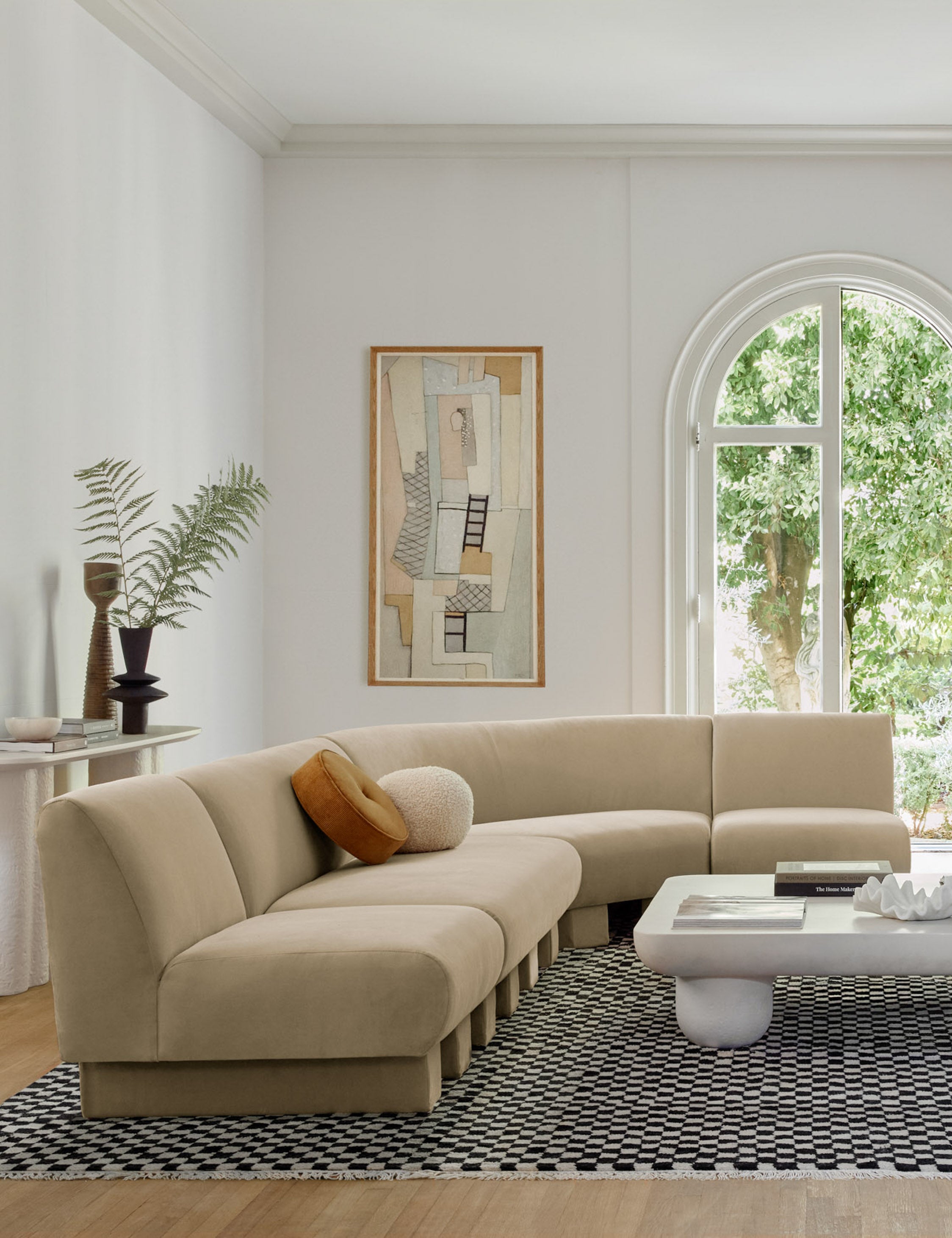 The Lena right-facing beige velvet sectional sofa with upholstered beam legs sits in a sculptural living room with a rounded coffee table and a boucle accent chair atop a black and white checkered rug.