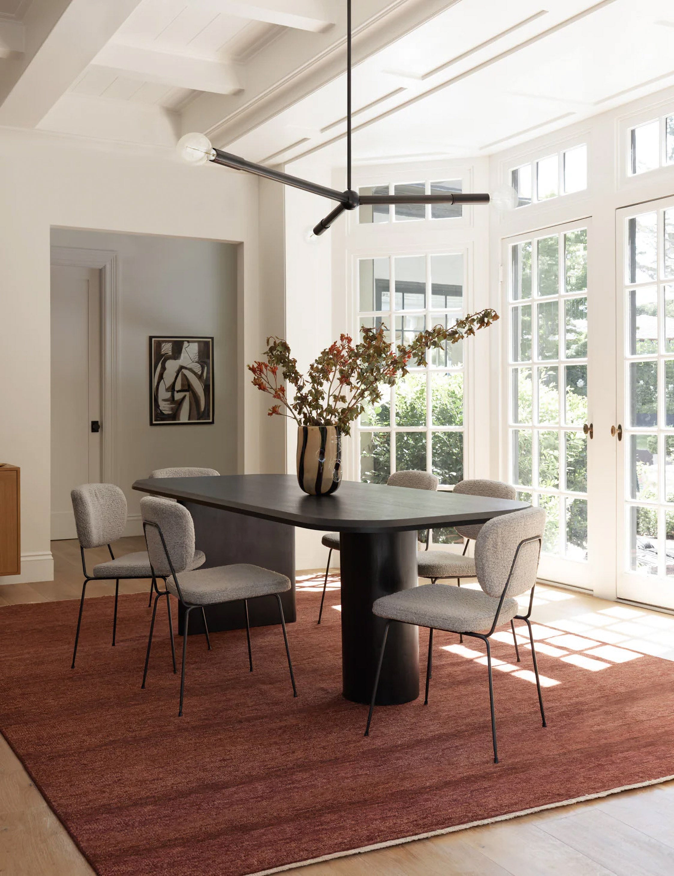 Archer Black Rectangular Dining Table sits in dining room atop a burgundy rug surrounded by gray cushioned dining chairs