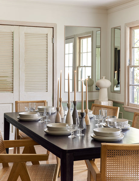 #color::black #size::82-W | The Reese black mango wood rectangular dining table sits in a dining room surrounded by woven dining chairs with wooden candles and white dinnerware on its surface.