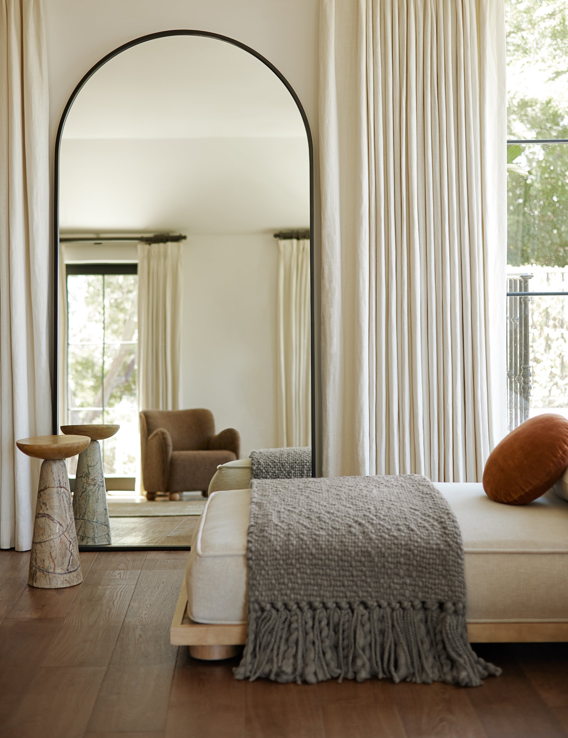 Idris thin metal framed floor length mirror in black styled next to a table and daybed