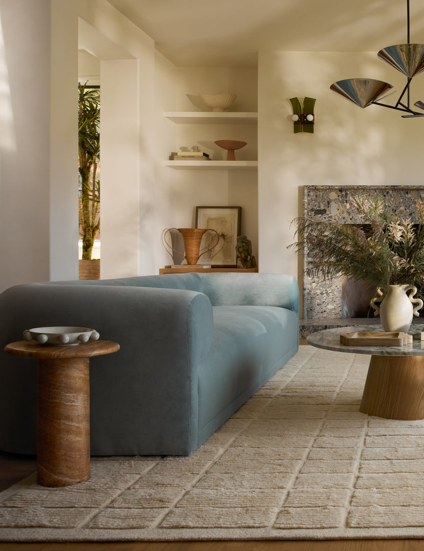 #color::Canyon-Faux-Travertine | Mona round stone drink table styled next to a blue velvet sofa.