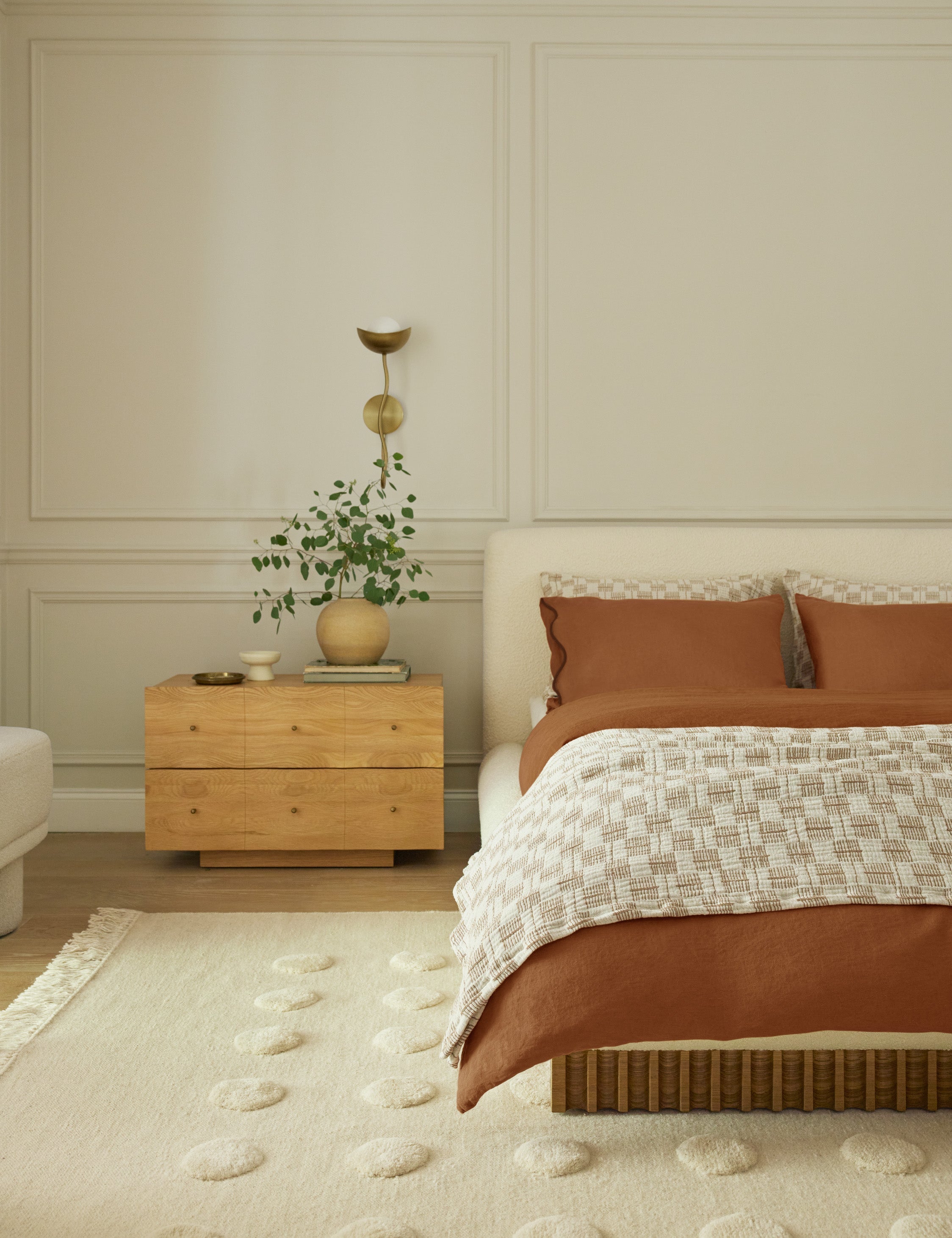 Kukka modern wavy arm wall sconce in brass hung above a large nightstand in a bedroom