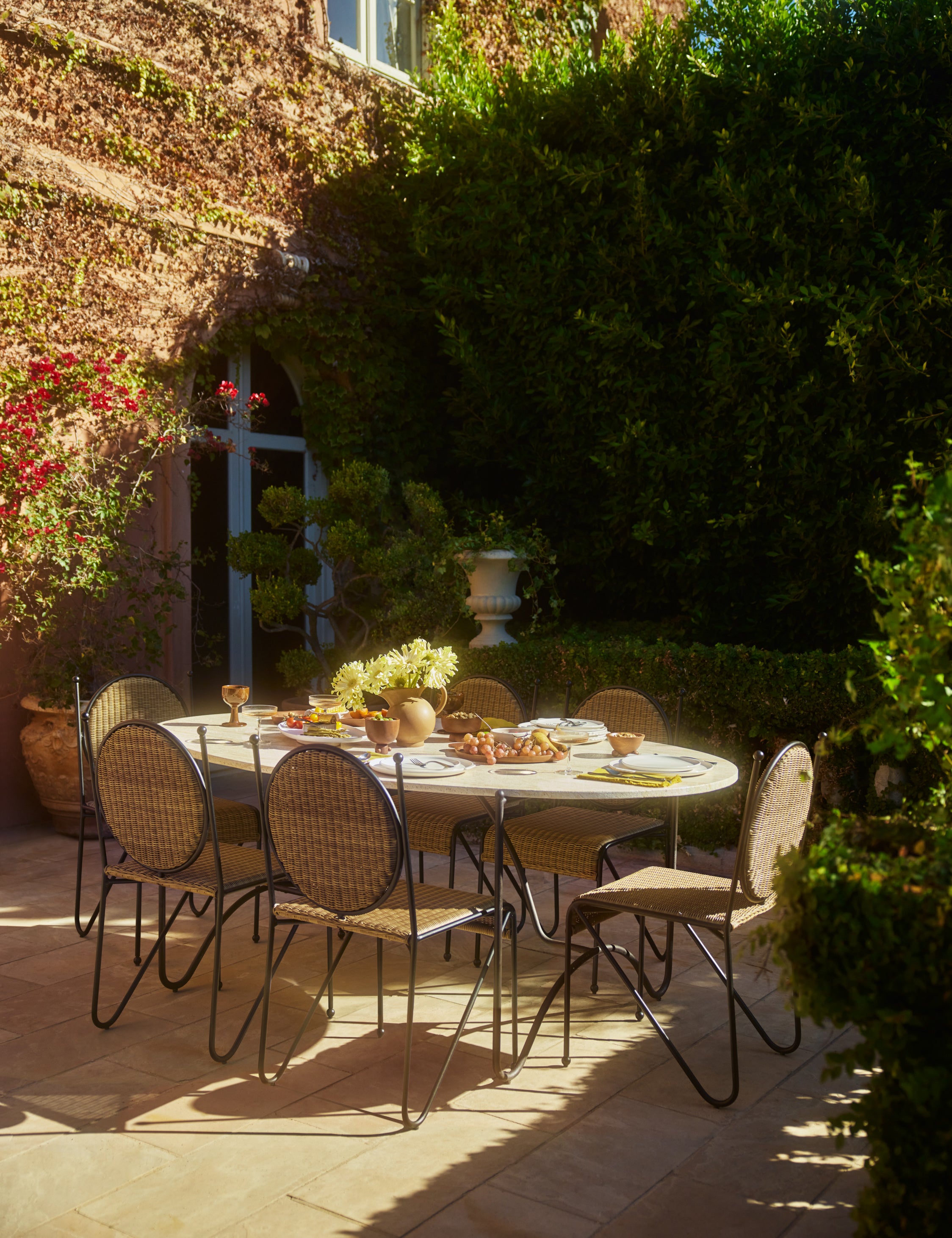 Six Ziggy modern wicker outdoor dining chair by Sarah Sherman Samuel placed around an oval outdoor dining table.