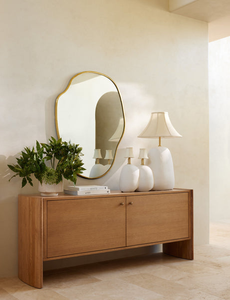 #color::gold #size::large | The large puddle mirror hangs on a cream wall over a wooden sideboard that has three sculptural lamps atop it