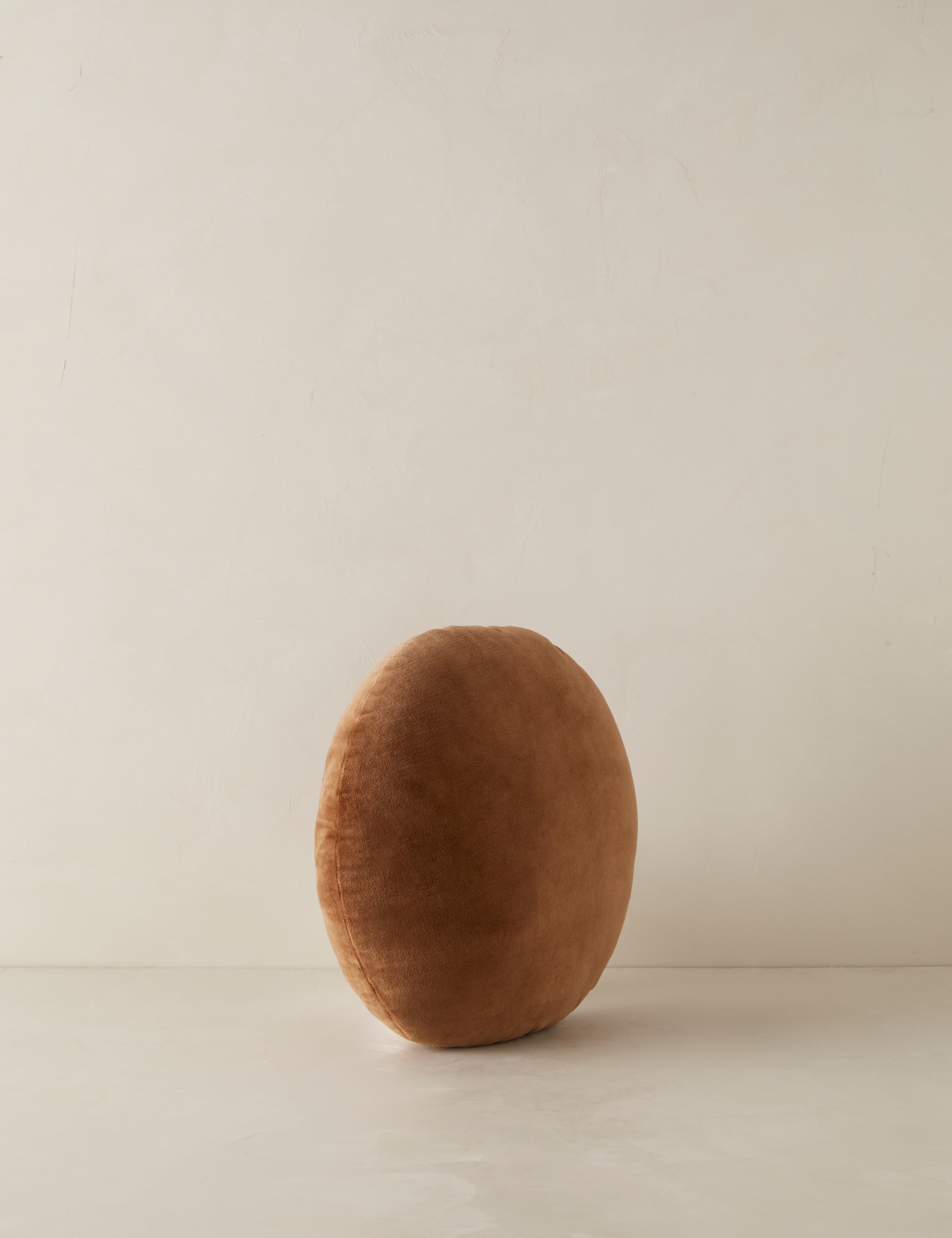Angled view of the Velvet round accent pillow in rust umber