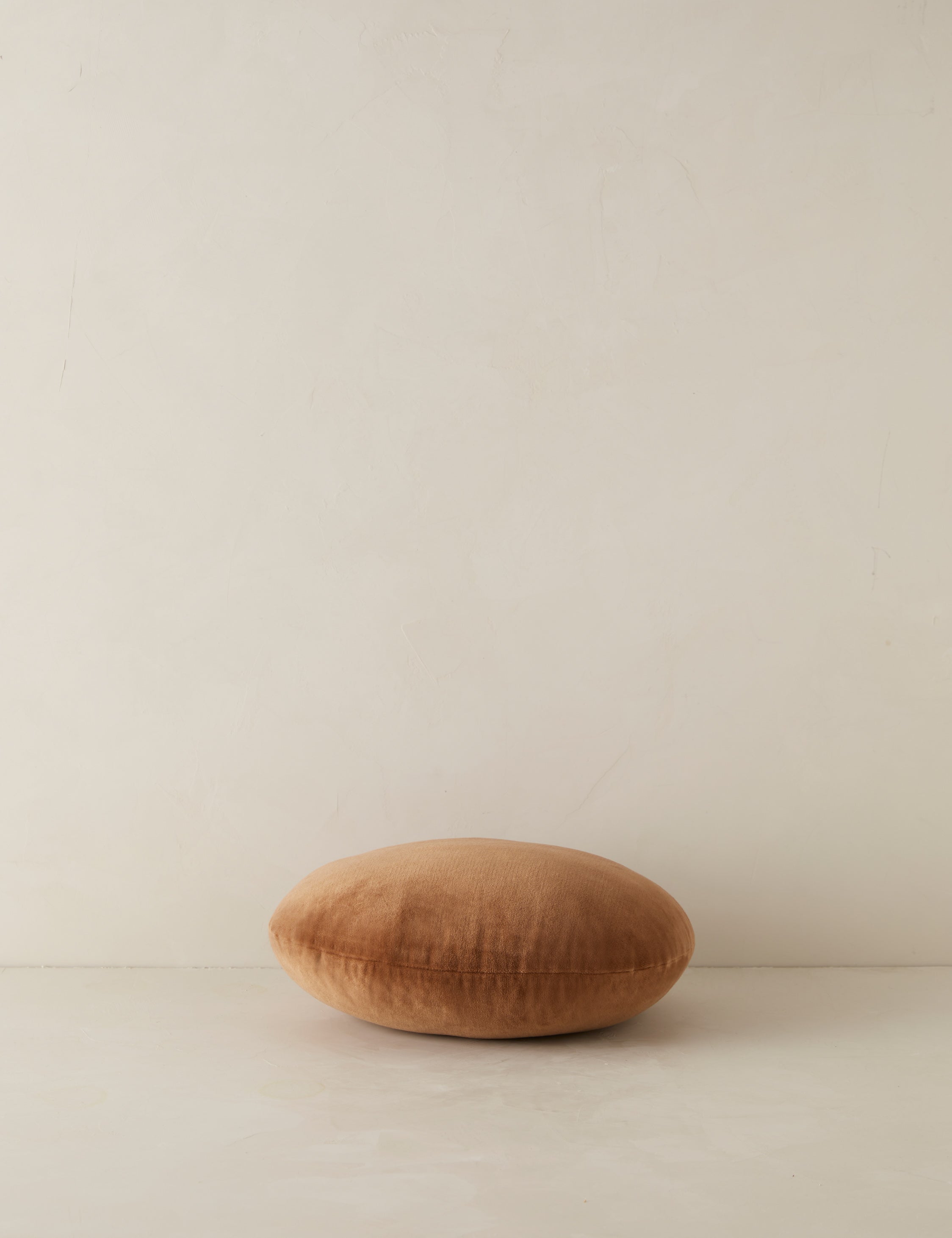 Velvet round accent pillow in rust umber laying flat