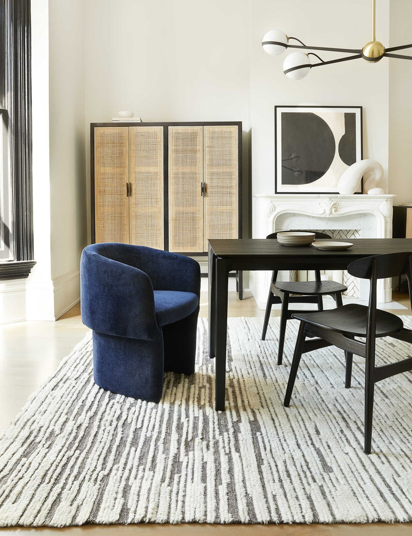 #color::black-and-natural | The Hannah black mango wood cabinet with cane doors sits in a dining room with black dining furniture and a navy velvet dining chair at the head of the table.