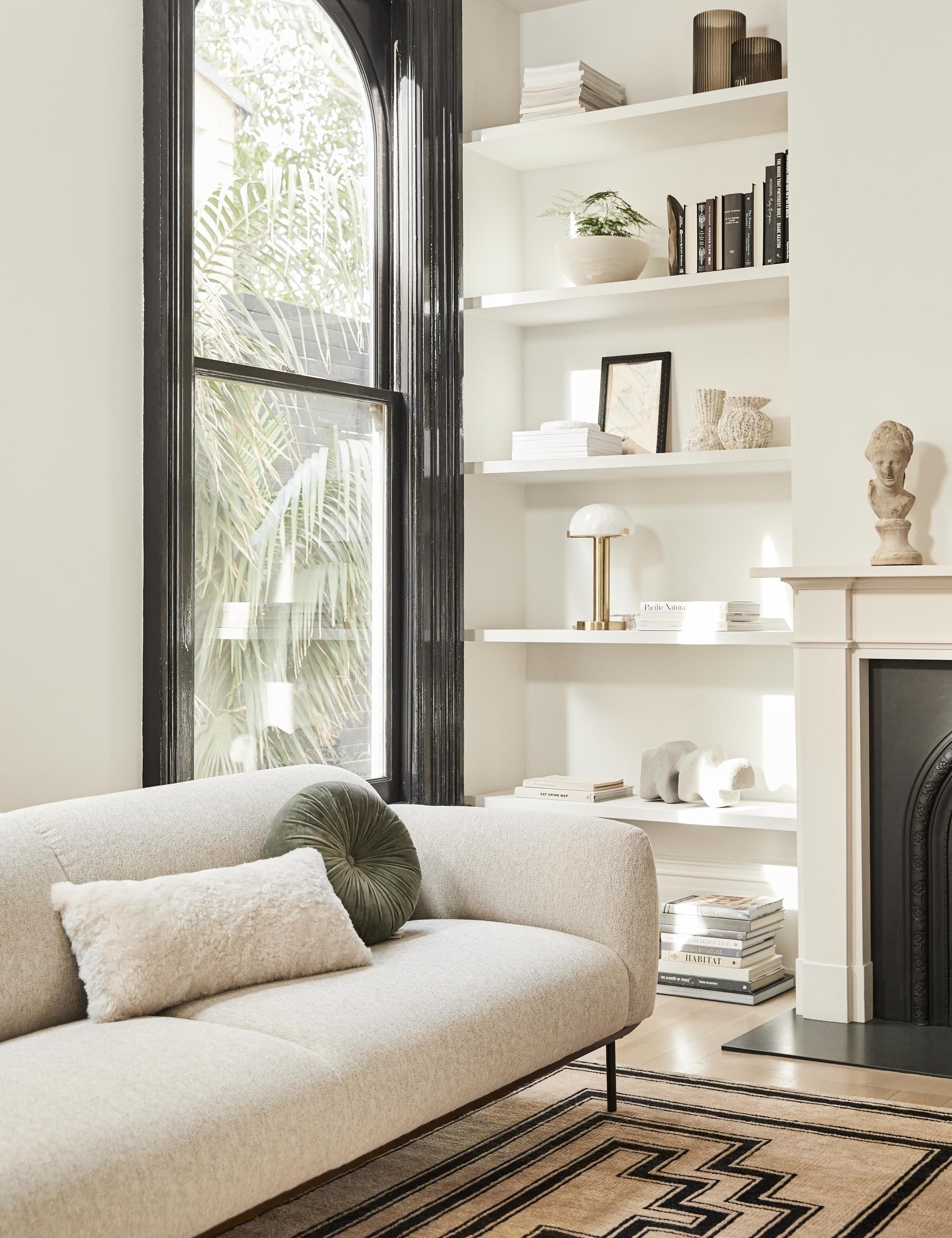 The Lelani table lamp with half-moon shade on a gold base sits in a living room on a shelf with various sculptural objects