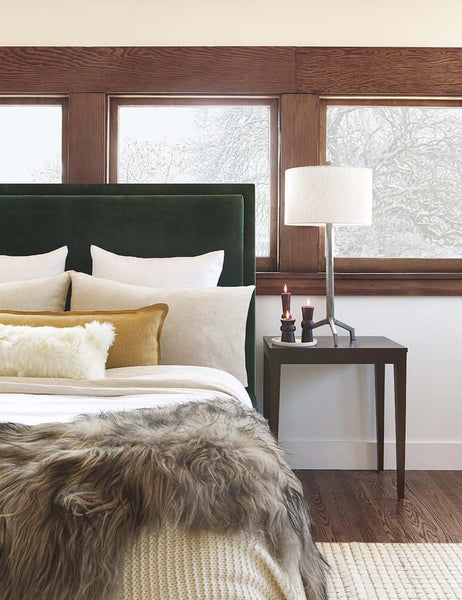 #color::marigold #style::extra-long #fill type::with-feather-down-insert #fill type::pillow-cover-only | The arlo marigold long lumbar pillow sits on an emerald green framed bed with ivory linens