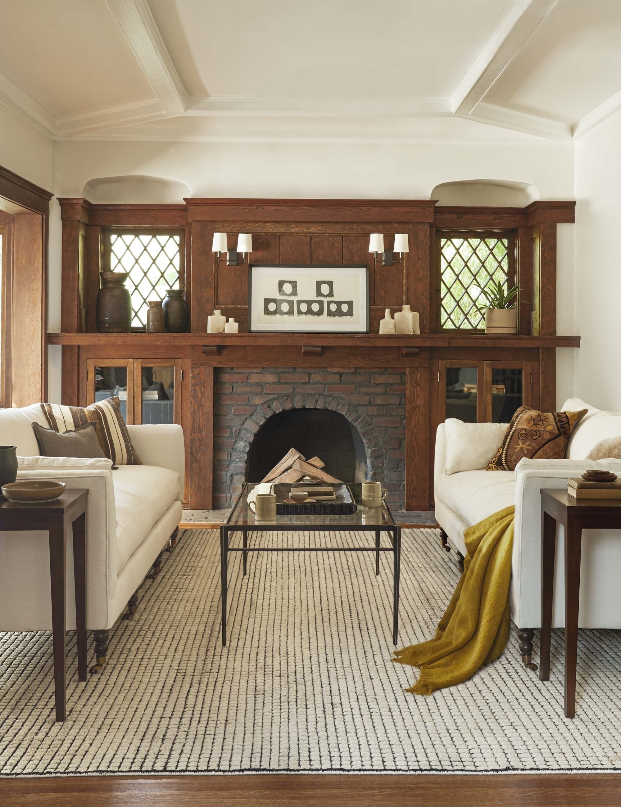 The Uma black and natural checkered grid pattern rug lays in a rustic living room under two cream sofas and a glass-top coffee table