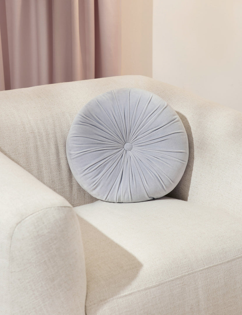 #color::ice-blue | The Monroe ice blue velvet round pillow sits on a white accent chair