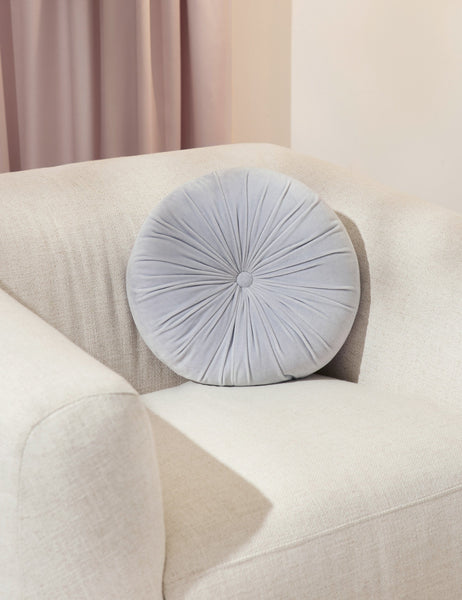 #color::ice-blue | The Monroe ice blue velvet round pillow sits on a white accent chair