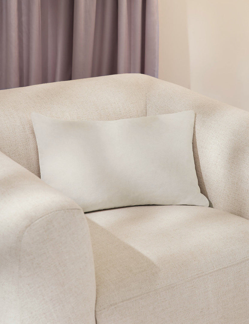 #color::oyster #style::lumbar  #fill type::with-feather-down-insert  #fill type::pillow-cover-only |   Charlotte oyster white lumbar velvet pillow sits on a white accent chair with a purple curtain in the background