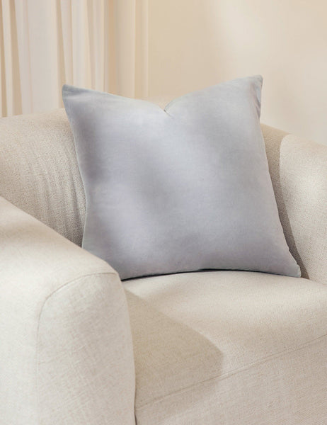 #color::ice-blue #size::20--x-20- #style::square  #fill type::with-feather-down-insert  #fill type::pillow-cover-only |   Charlotte ice blue square velvet pillow sits on a white accent chair with a white curtain in the background