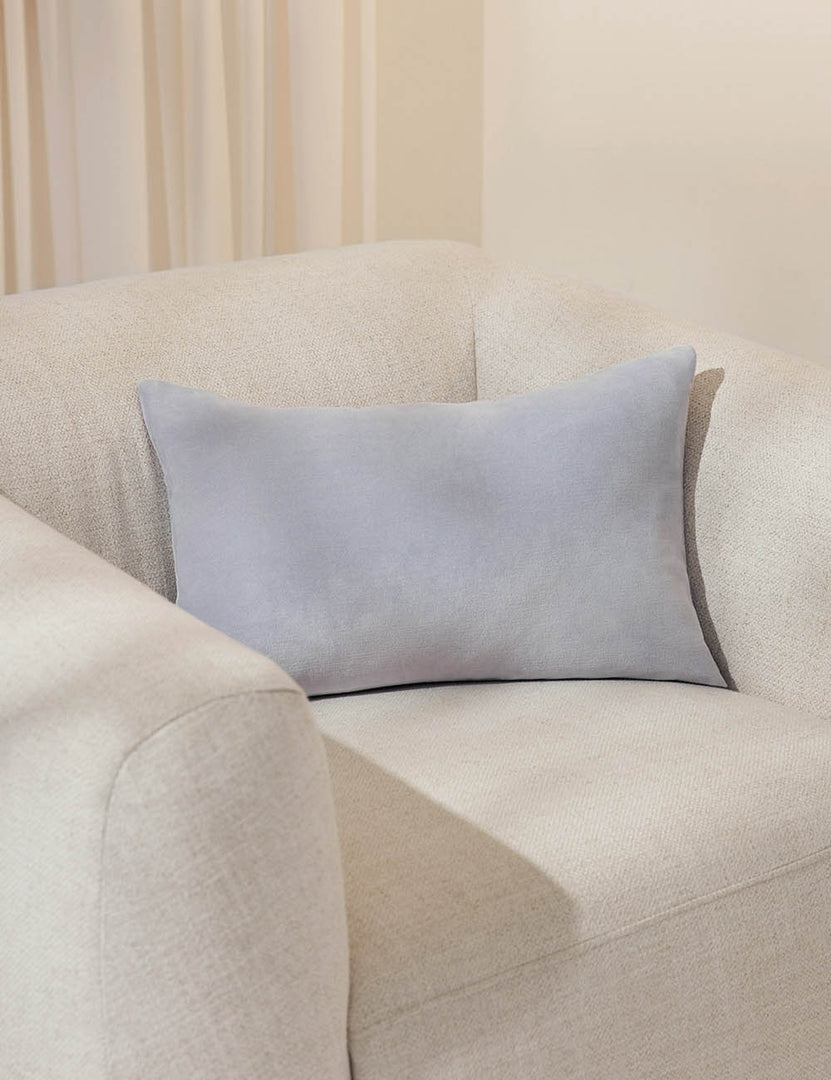 #color::ice-blue #size::13--x-20- #style::lumbar #fill type::with-feather-down-insert  #fill type::pillow-cover-only |   Charlotte ice blue lumbar velvet pillow sits on a white accent chair with a white curtain in the background
