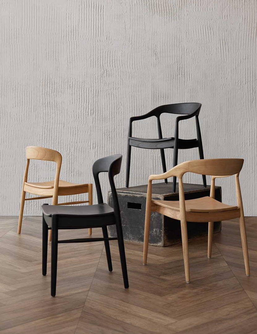 #color::natural | Two Natural and Two Black Ida Dining Arm Chairs sit in a room with a black wooden box, a textured wall, and chevron wooden floors