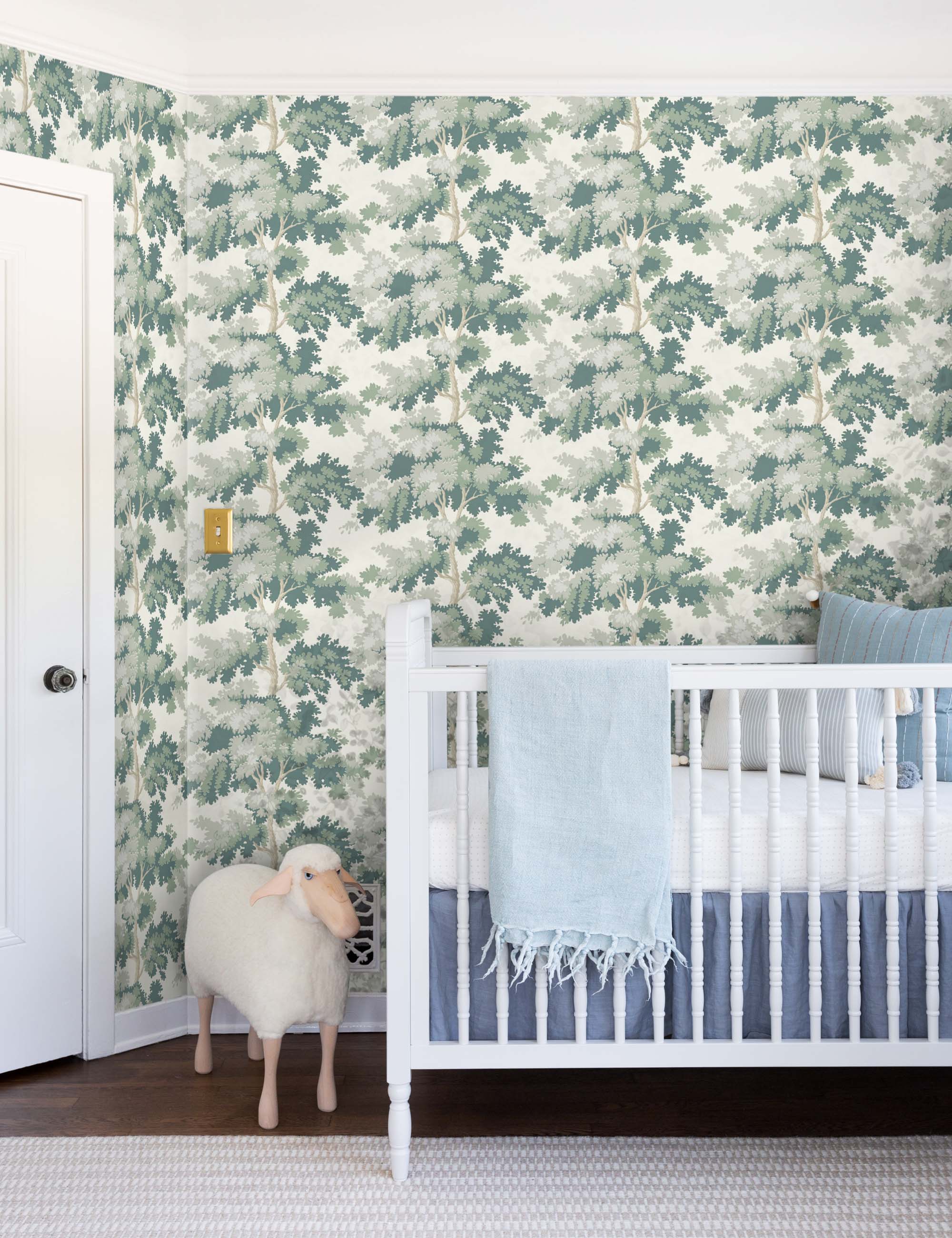 The Scalamandre botanical inspired green raphael wallpaper is in a nursery with a white crib and a toy lamb