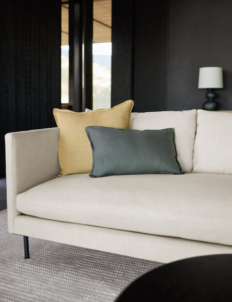 #color::conifer #style::lumbar #fill type::with-feather-down-insert #fill type::pillow-cover-only | The arlo conifer gray lumbar pillow sits on a natural linen sofa with a light yellow linen pillow