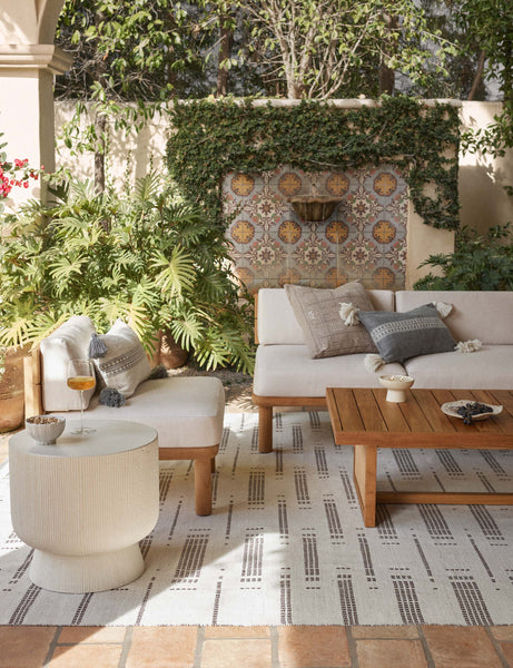 #color::agate #style::lumbar #color::natural-and-agate #style::lumbar | Marchesa agate and agate and natural indoor and outdoor pillow with tasseled corners sit on sofa in an outdoor space with a wooden coffee table