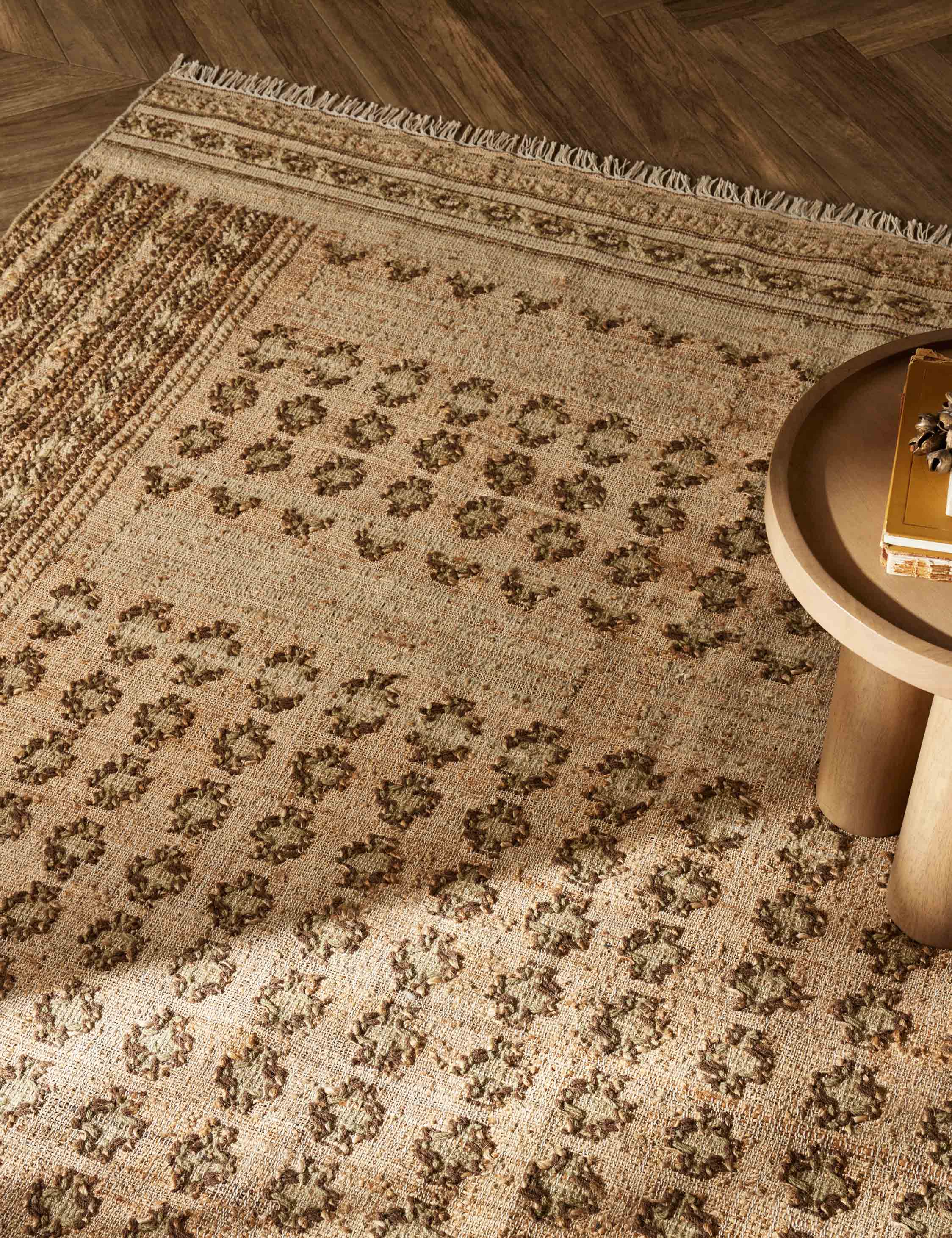 Close-up of the Keziah moss rug under a round side table with pedestal legs