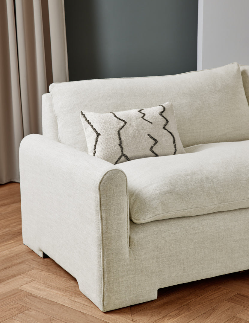 #color::natural-linen | The Rupert natural linen sofa sits in a studio room with an ivory flatweave pillow with black accents sitting atop it