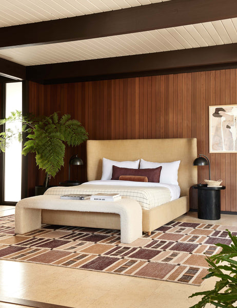 #color::black | The Luna black wood round side table sits next to a camel linen framed bed and a red, orange, and natural patterned rug 