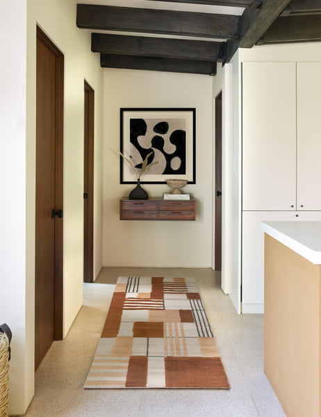 #size::2-6--x-8- | The Benita natural toned hand-knotted floor rug by Nina Freudenberger in its runner size lays in a hallway with a wooden shelf, a black sculptural vase, and an abstract wall art