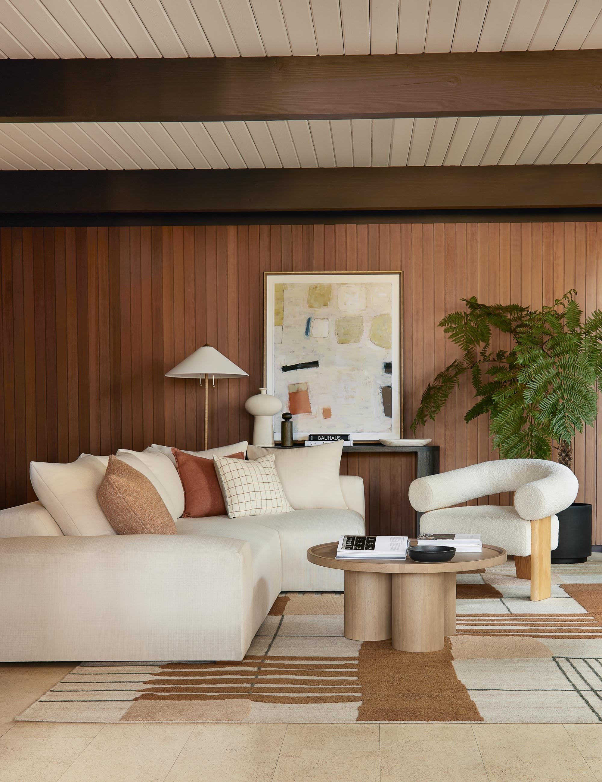 The Benita natural toned hand-knotted floor rug by Nina Freudenberger lays in a living room with a natural linen sofa, a white boucle accent chair, and a wooden circular coffee table