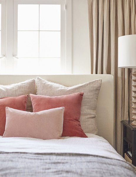 #color::rosewater #style::lumbar  #fill type::with-feather-down-insert  #fill type::pillow-cover-only |   Charlotte rosewater pink square velvet pillow sits on a neutral linen framed bed with striped linens and dark pink throw pillows