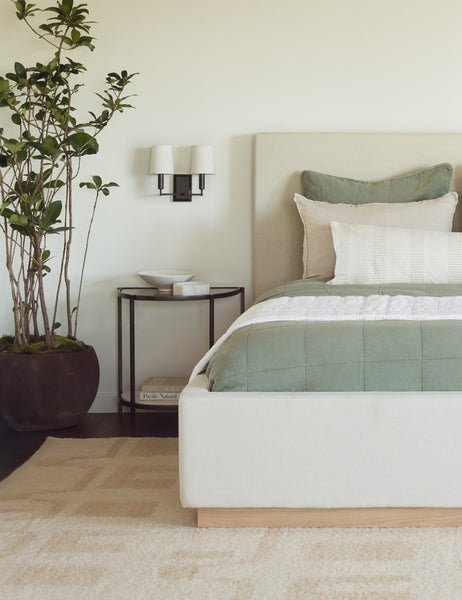 #color::dark-bronze | The Charlie dark bronze double sconce with parchment shades and angular arms is mounted in a bedroom with a natural linen bed, a plush natural-toned rug, and sage-toned accent pillows and throws