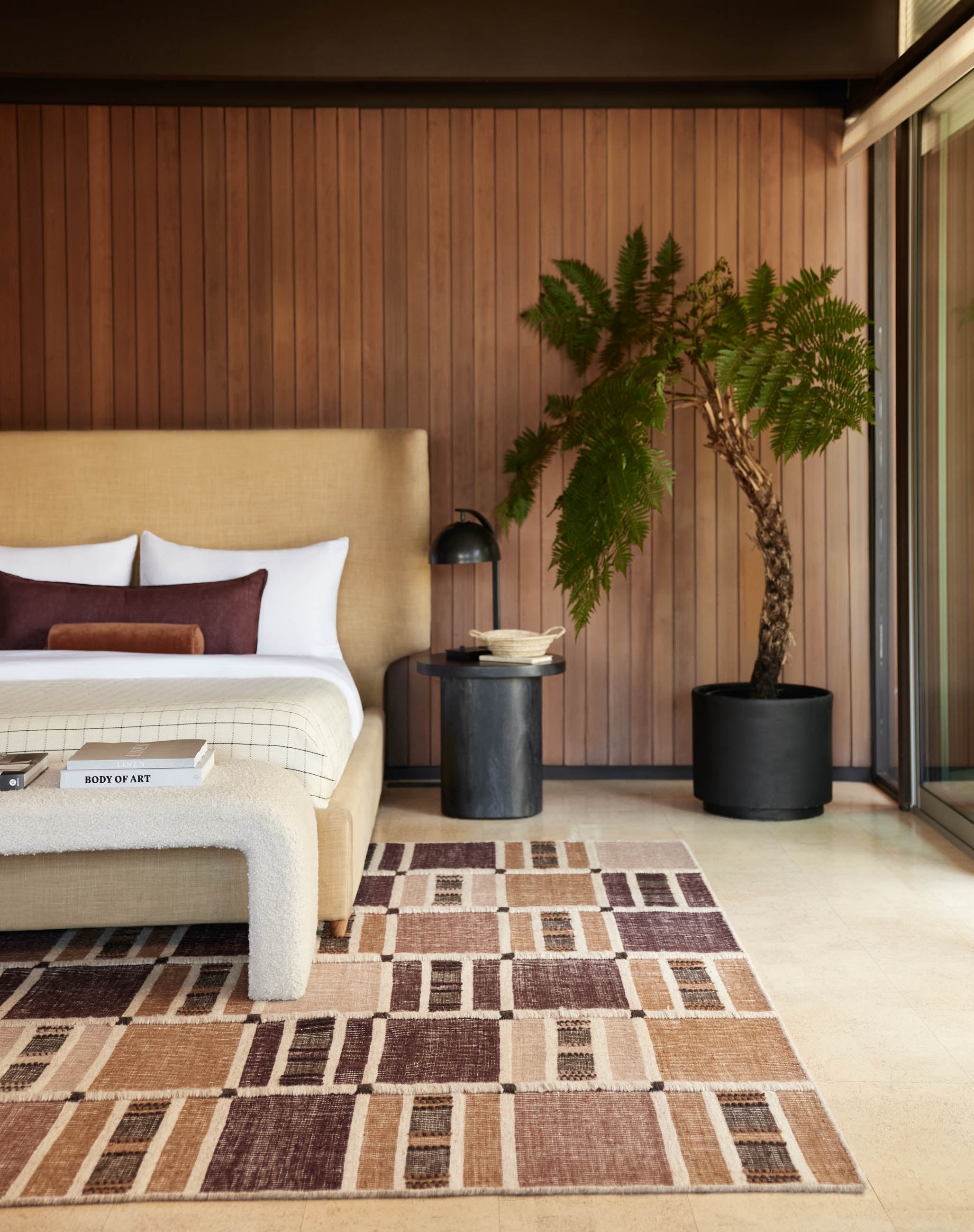 The Anni rug lays in a retro room with wood-paneled walls under a golden linen framed bed with white and burgundy linens