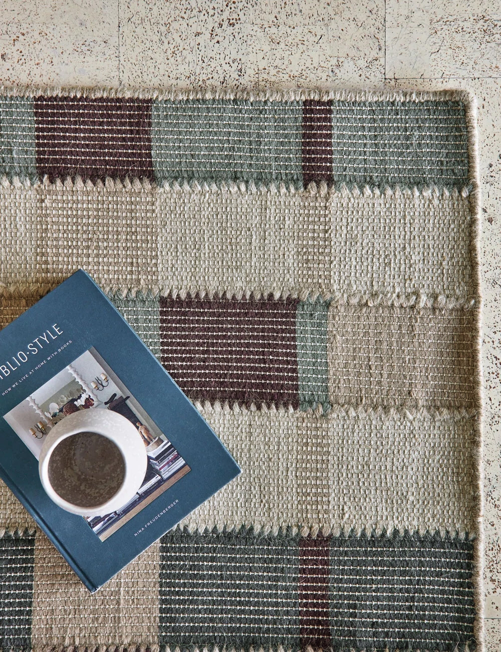 The corner of the Marli Rug under a ceramic mug and a blue book