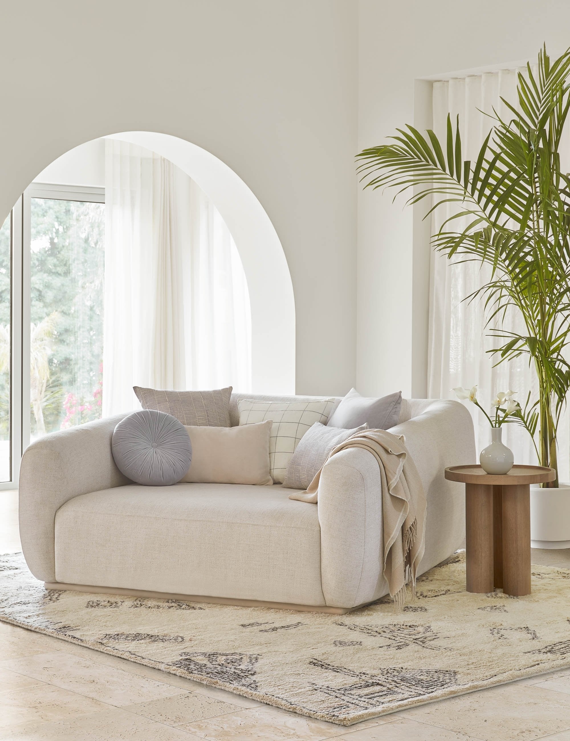 The Monroe ice blue velvet round pillow sits on a white accent chair