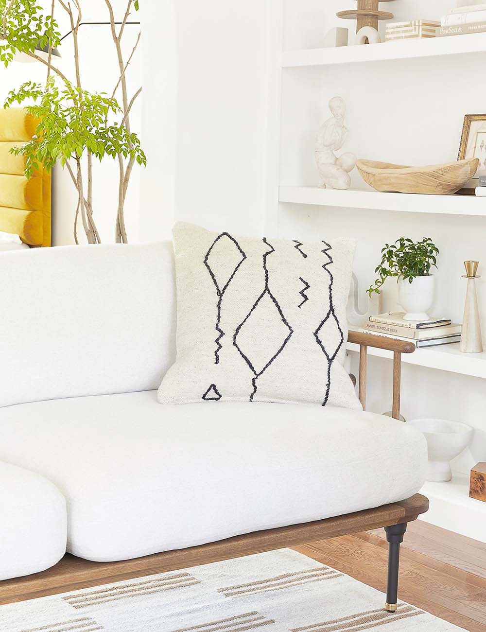 The moroccan black and natural beni ourain inspired square flat weave pillow by Sarah Sherman Samuel sits atop a white linen sofa