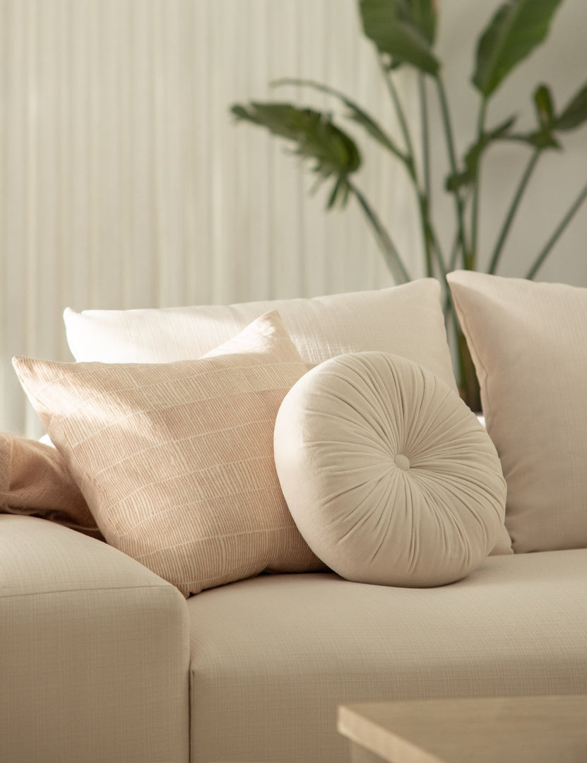 #color::oyster | The Monroe oyster white velvet round pillow sits on a white accent chair