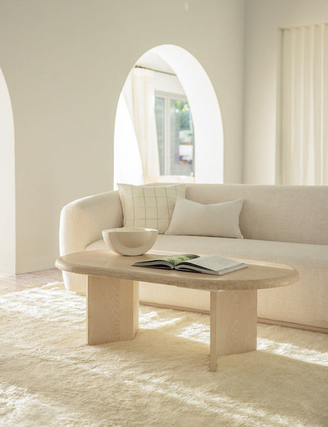 #color::oyster #style::lumbar  #fill type::with-feather-down-insert  #fill type::pillow-cover-only |   Charlotte oyster white lumbar velvet pillow sits on a cream sofa behind a light wooden oval coffee table
