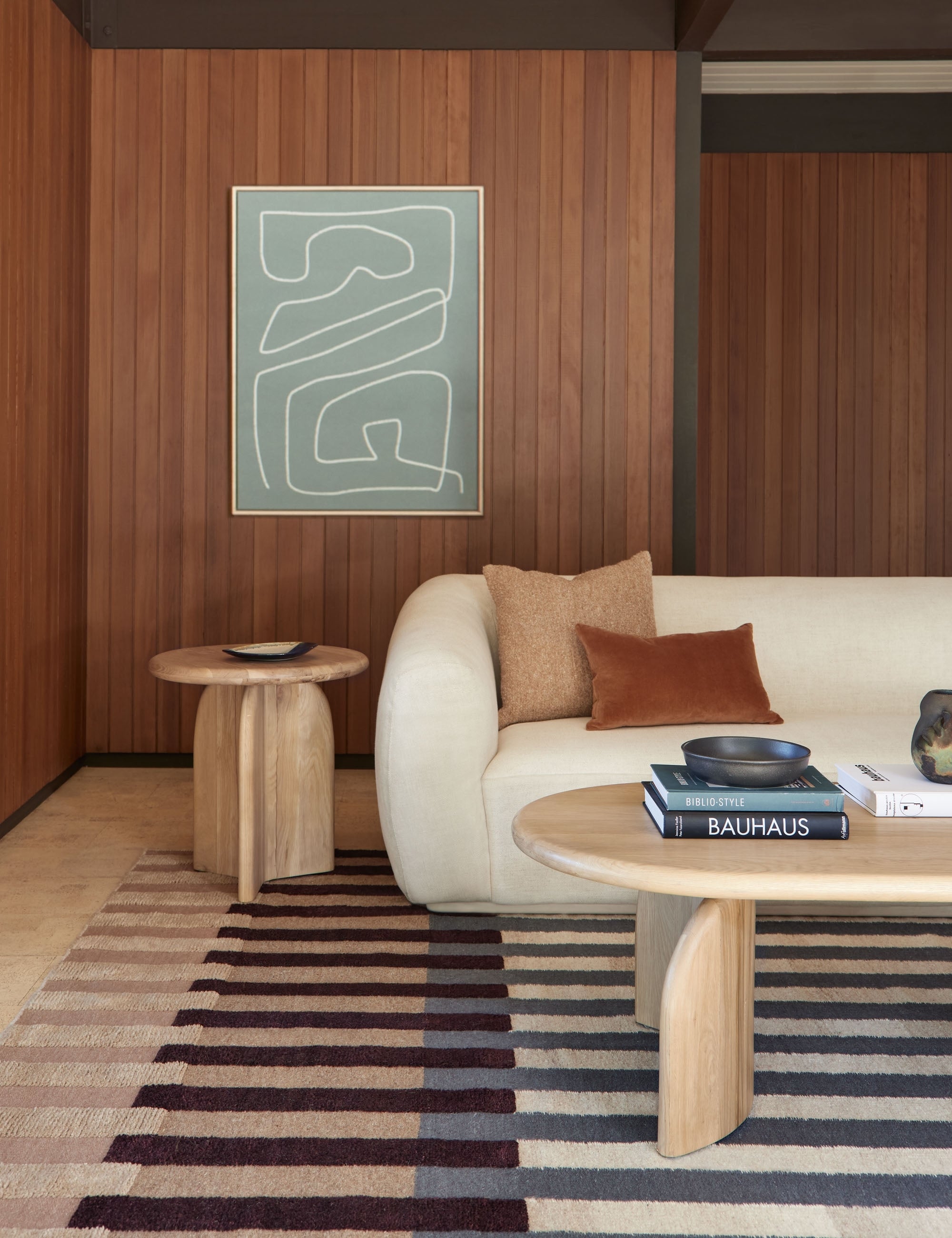 The otti rug lays in a retro living room under an oval coffee table, a round side table, and an ivory boucle sofa