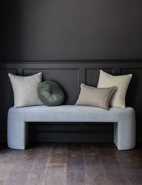 #color::moss | The Monroe moss green velvet round pillow sits on a light blue velvet bench with other throw pillows in a room with black walls