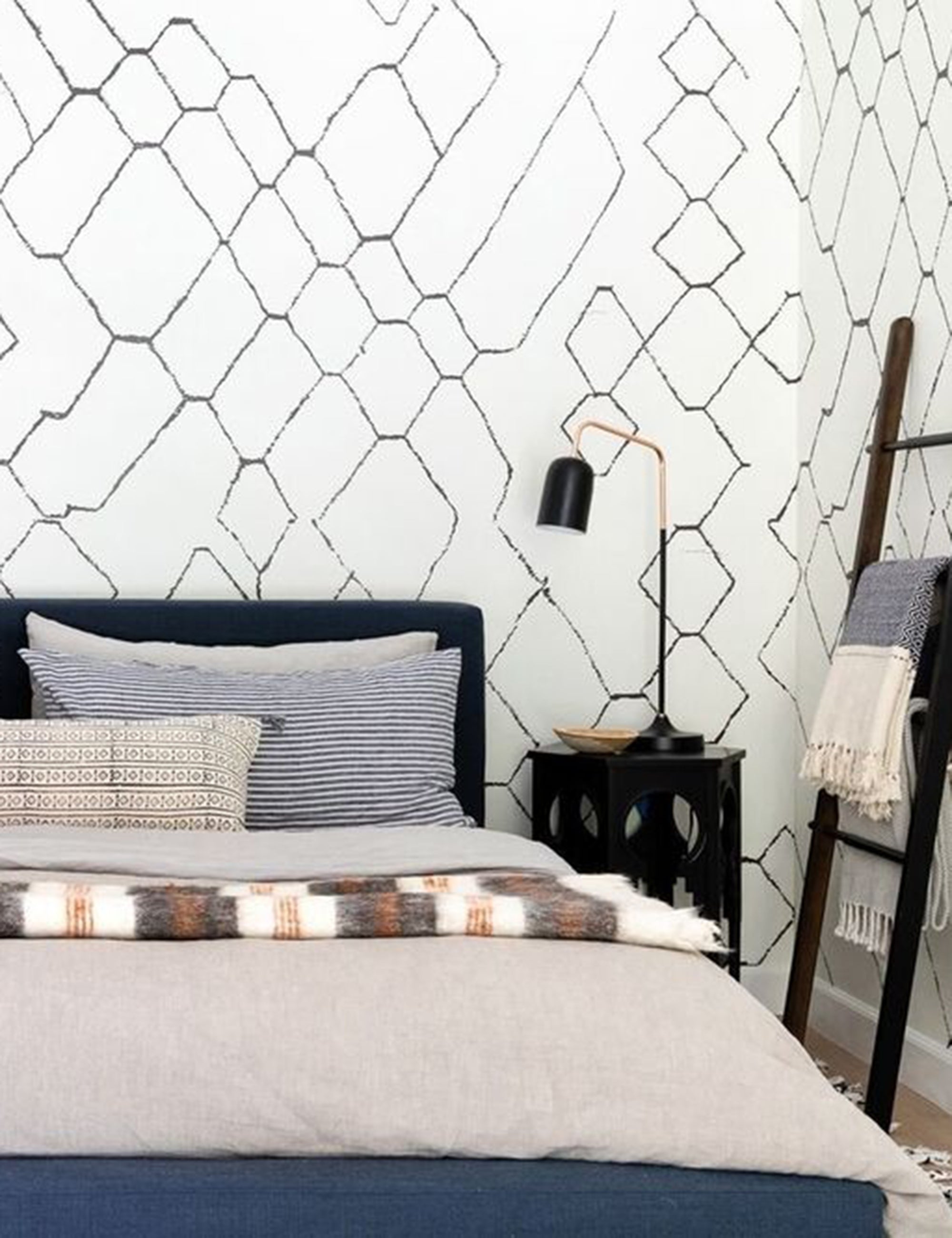 The European Flax Linen smoke gray Duvet Set by Cultiver lays on a dark framed bed in a bedroom with white and black geometric patterned walls, a sculptural black nightstand, and patterned throw pillows
